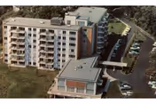 Aerial view of a multi-story apartment building with balconies, a parking lot, and a covered walkway to a smaller adjoining structure.