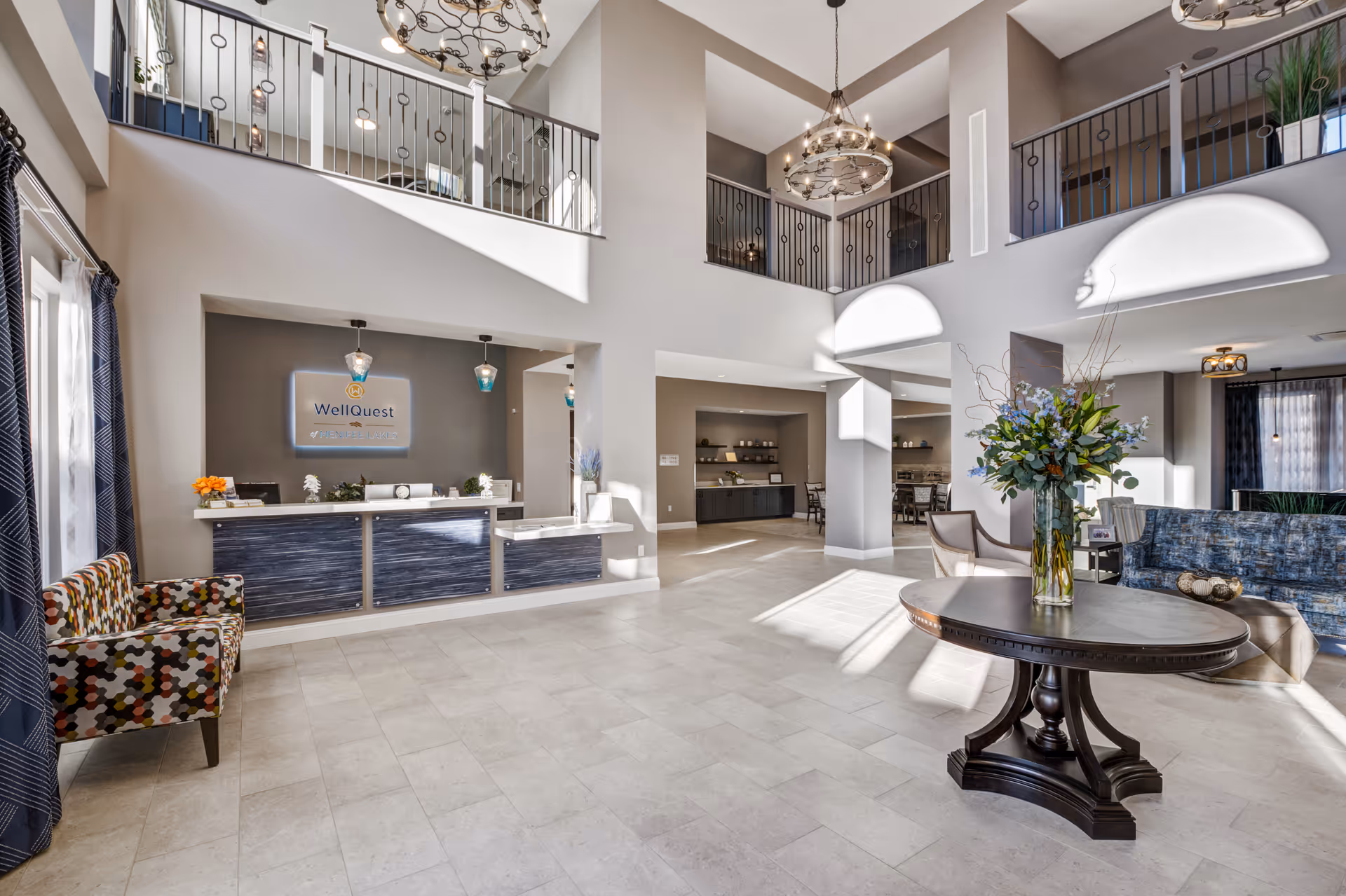 Spacious two-story reception lobby with a front desk, seating areas, a round table with flowers, and an open balcony above.