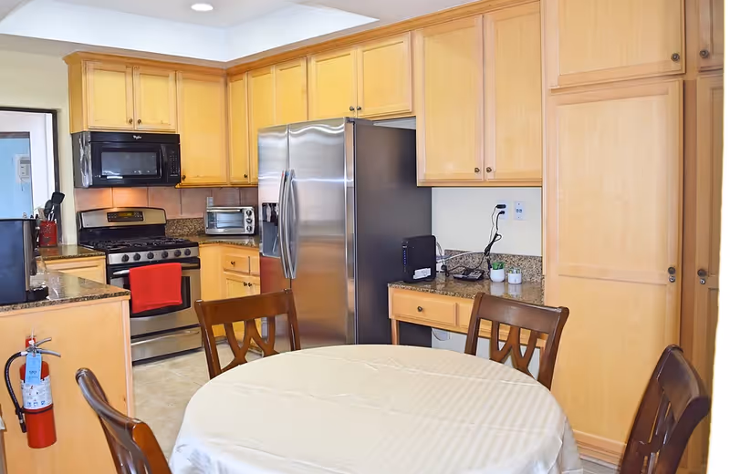 Bright kitchen with wooden cabinets, stainless steel appliances, and a round table with chairs in the foreground.