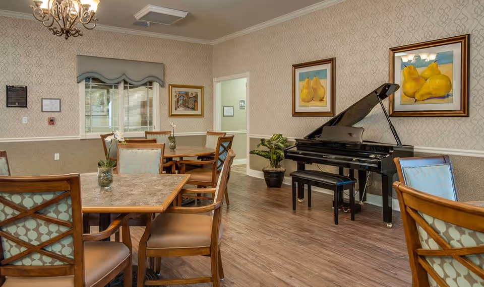 A senior living dining/activity room with wooden tables and chairs and a black grand piano against patterned wallpaper.