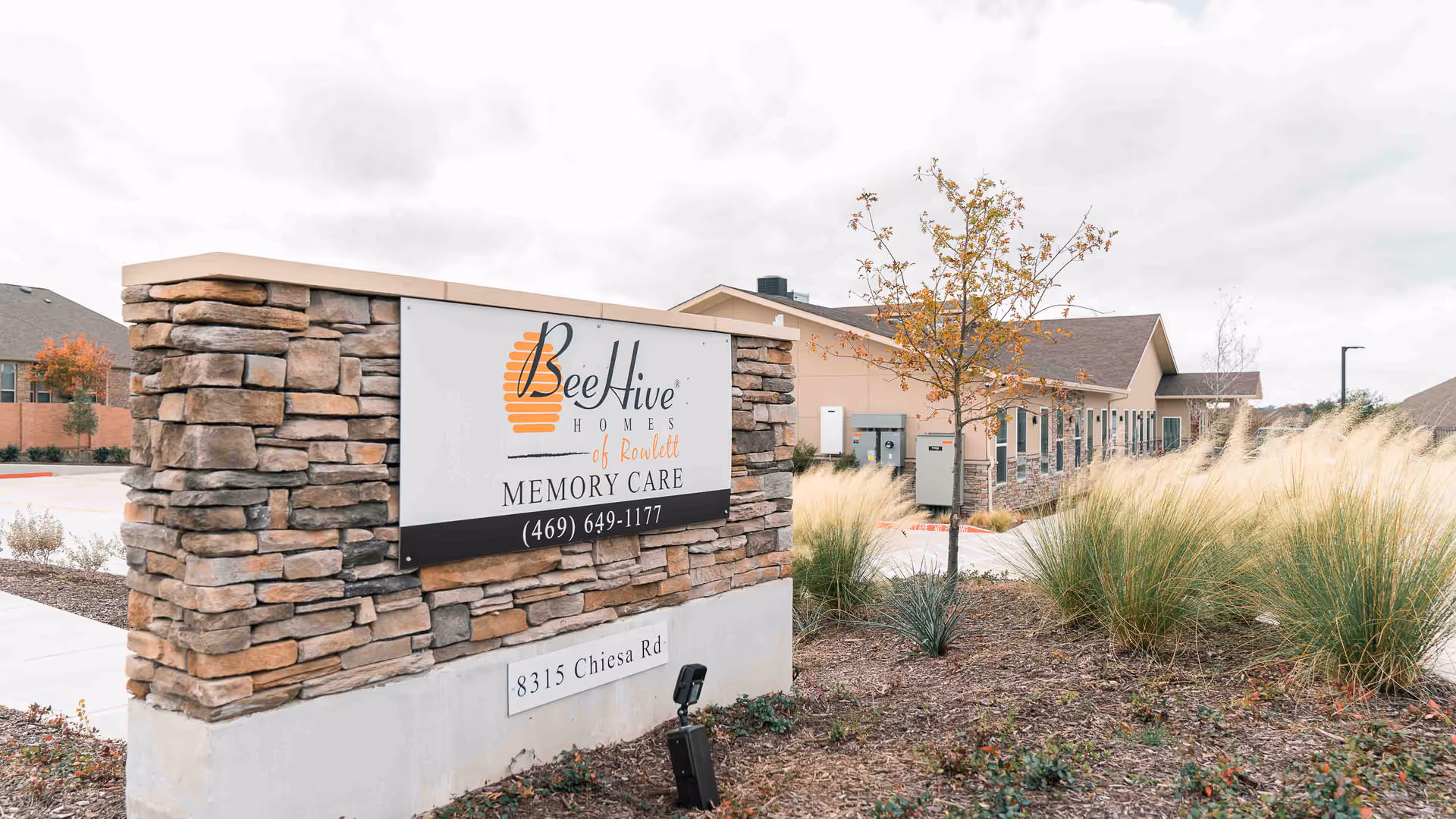 Stone sign reading 'BeeHive Homes of Rowlett Memory Care' in front of the facility building and landscaped grounds.
