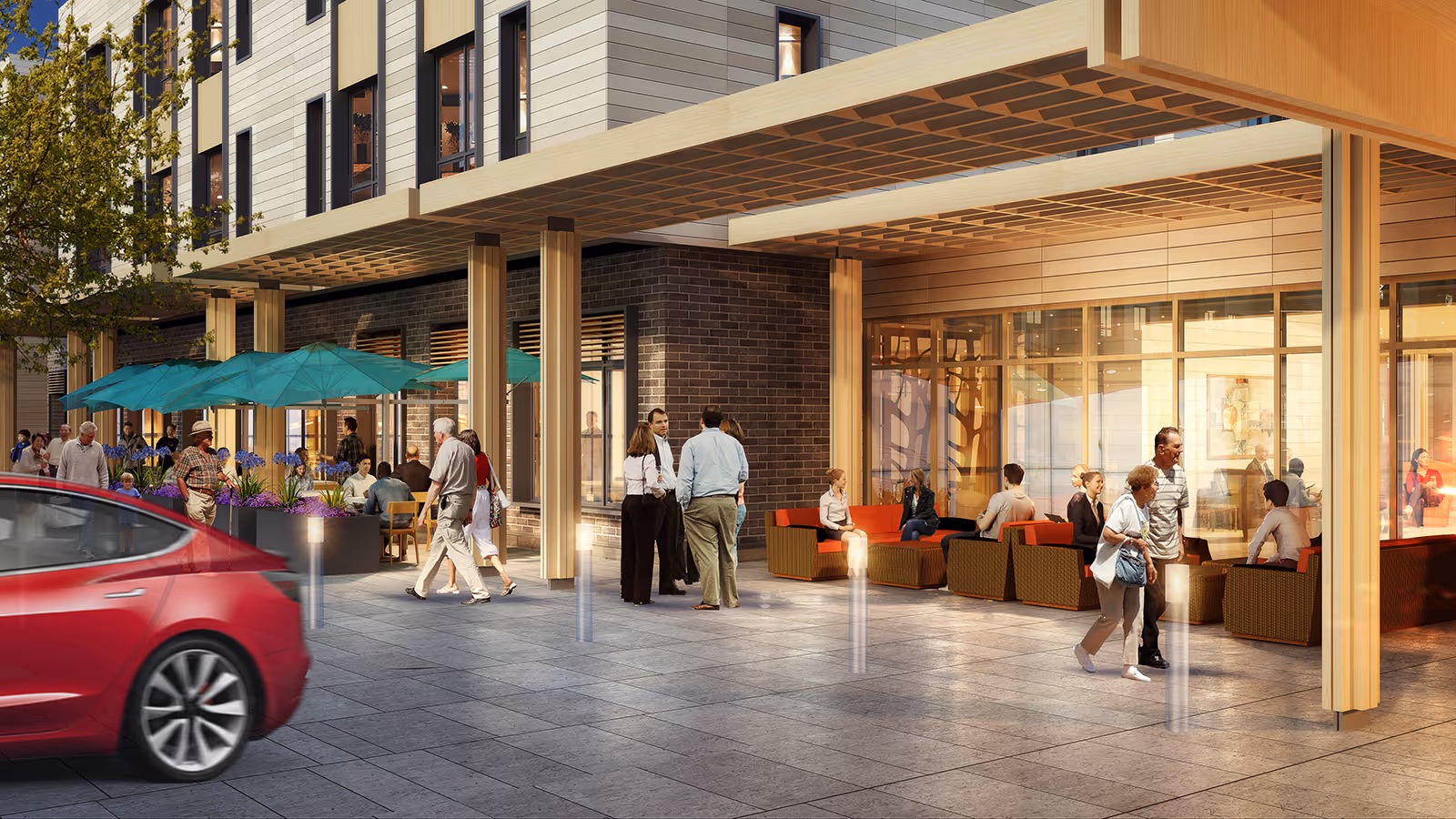 Outdoor patio area of The Baldwin Senior Living with people walking and sitting under teal umbrellas and on orange cushioned chairs. The building exterior features large windows and wooden pillars.