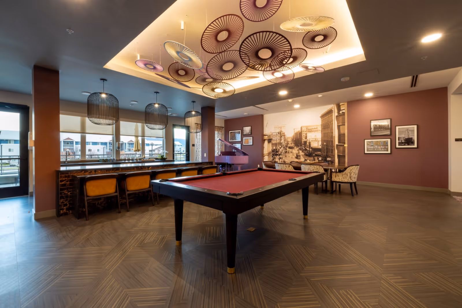 Community lounge with a red pool table, bar seating, decorative ceiling fixtures and a vintage mural on the far wall.