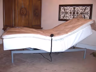 Adjustable hospital-style bed with raised head section and remote control in a furnished room.