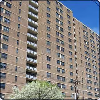 Tall brick senior living building with balconies, viewed from street against blue sky.