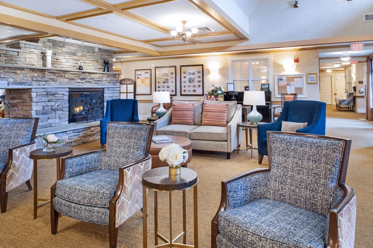 Comfortable senior living lounge with upholstered chairs, sofas, side tables, and a stone fireplace.