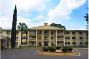 Three-story beige senior living building with balconies, palm trees, and a circular driveway.