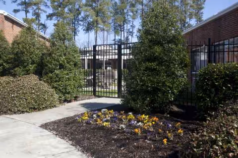 Gated entrance to Carver Rehabilitation & Living Center with shrubs and flower bed.