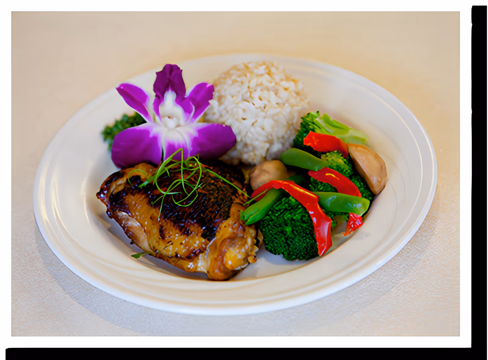 A white plate with a serving of grilled chicken, steamed white rice, and mixed vegetables including broccoli, snap peas, red bell peppers, and mushrooms, garnished with a purple orchid flower and green herbs.