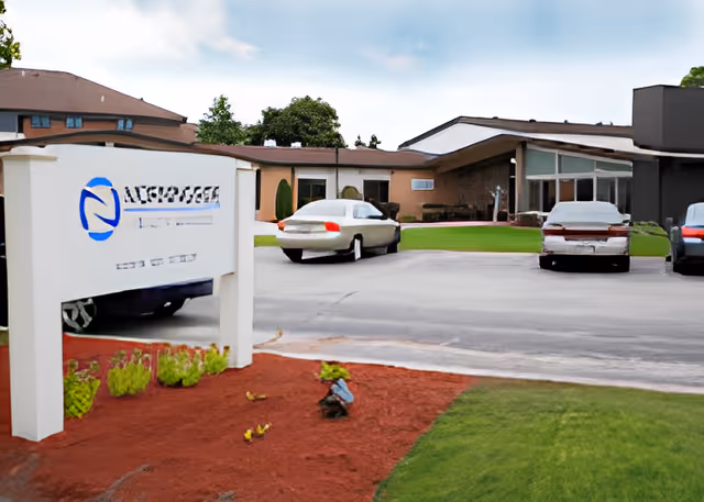 Exterior view of Morningside Health Services facility showing a parking area with several cars, a landscaped area with mulch and small plants, and a sign with the facility's name near the entrance.