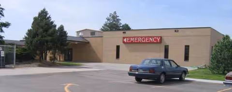 Exterior view of a hospital with an Emergency entrance and parked cars.