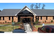 Brick senior living center with central entrance, walkway, and parked cars in front.