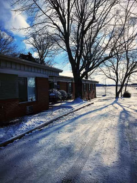Brick senior living building along a snow-covered driveway with bare trees in winter.