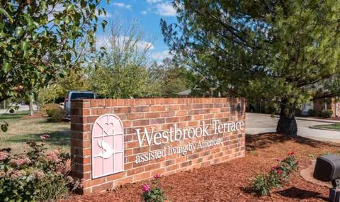 Brick sign displays Westbrook Terrace Assisted Living beside landscaped entrance.