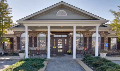 Front entrance of Etheridge House Senior Living with brick exterior, columns, and seating near the doors.