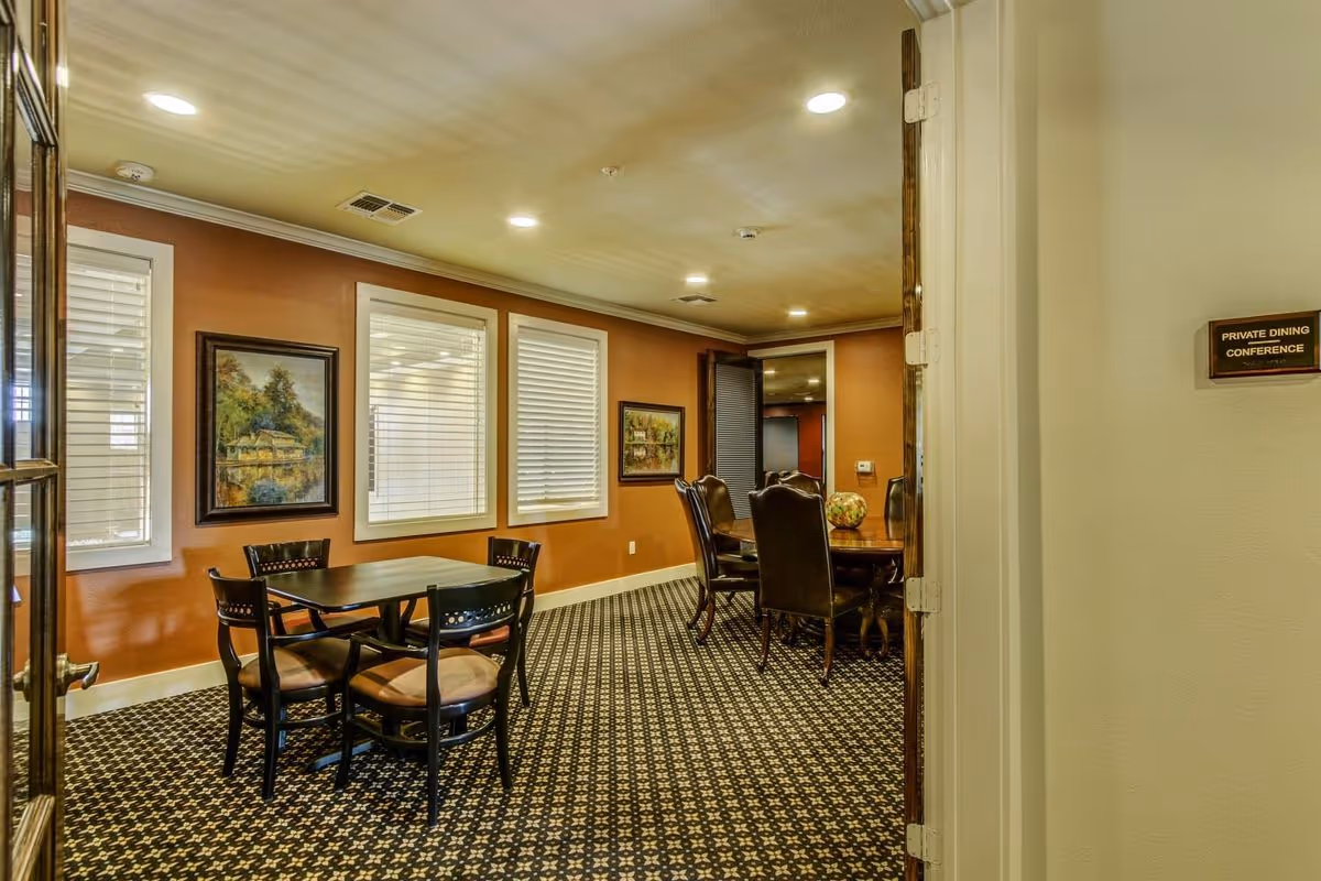 Interior view of a private dining/conference room with tables, chairs, framed artwork, and patterned carpet.