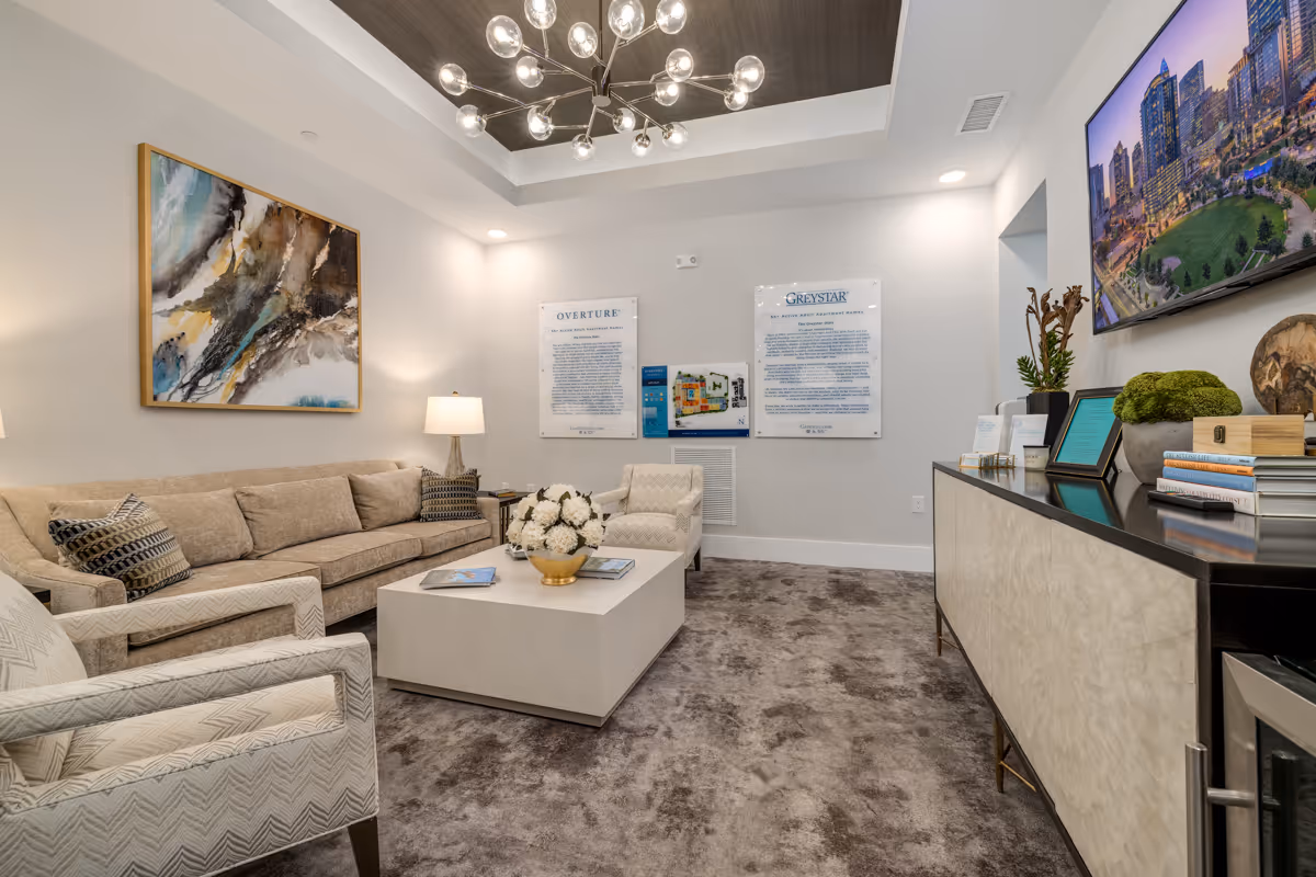 Bright furnished lounge with a beige sofa, armchairs, coffee table, wall art, informational wall signs and a modern chandelier.