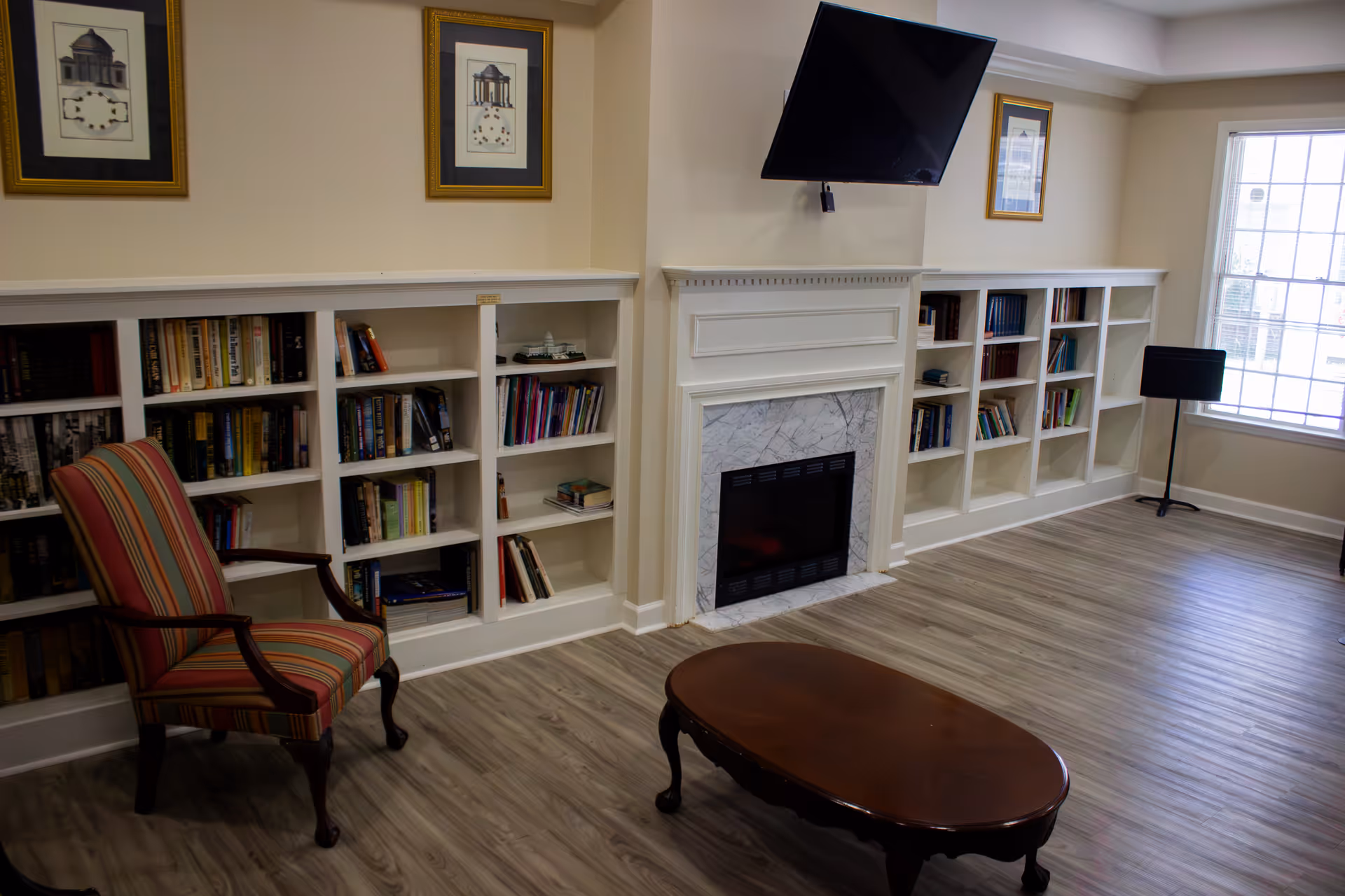 Common room with built-in bookshelves on either side of a fireplace, a wall-mounted TV, a striped armchair and a wooden coffee table.