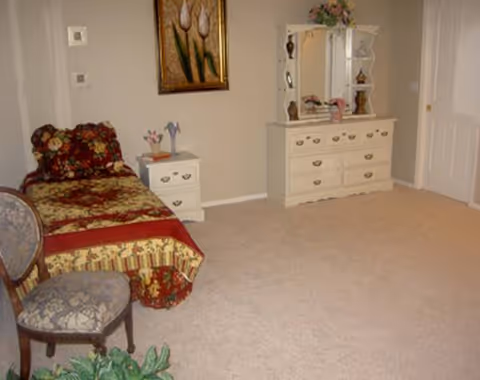 A bedroom with a bed, dresser with mirror, nightstand, chairs, and wall art.
