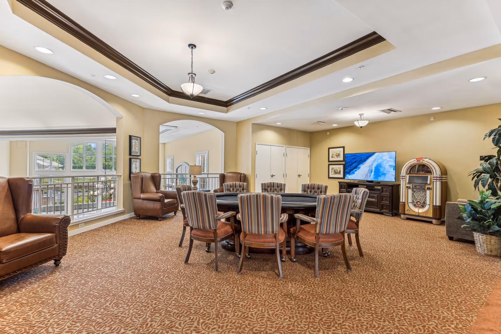 A bright communal lounge with a round card table and striped chairs, leather armchairs by large windows, a TV and vintage jukebox.