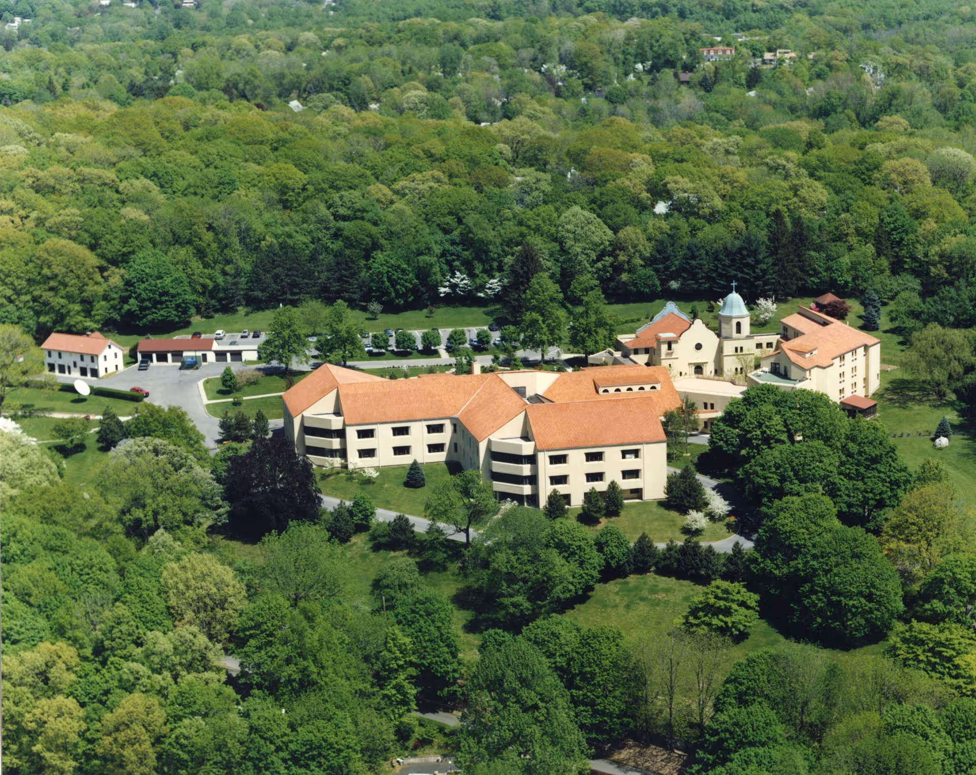 Aerial view of the Rosary Hill Home campus showing several connected red‑tiled buildings surrounded by trees and lawns.