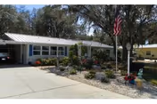 Single-story senior living home with a carport, flagpole, and landscaped front yard.