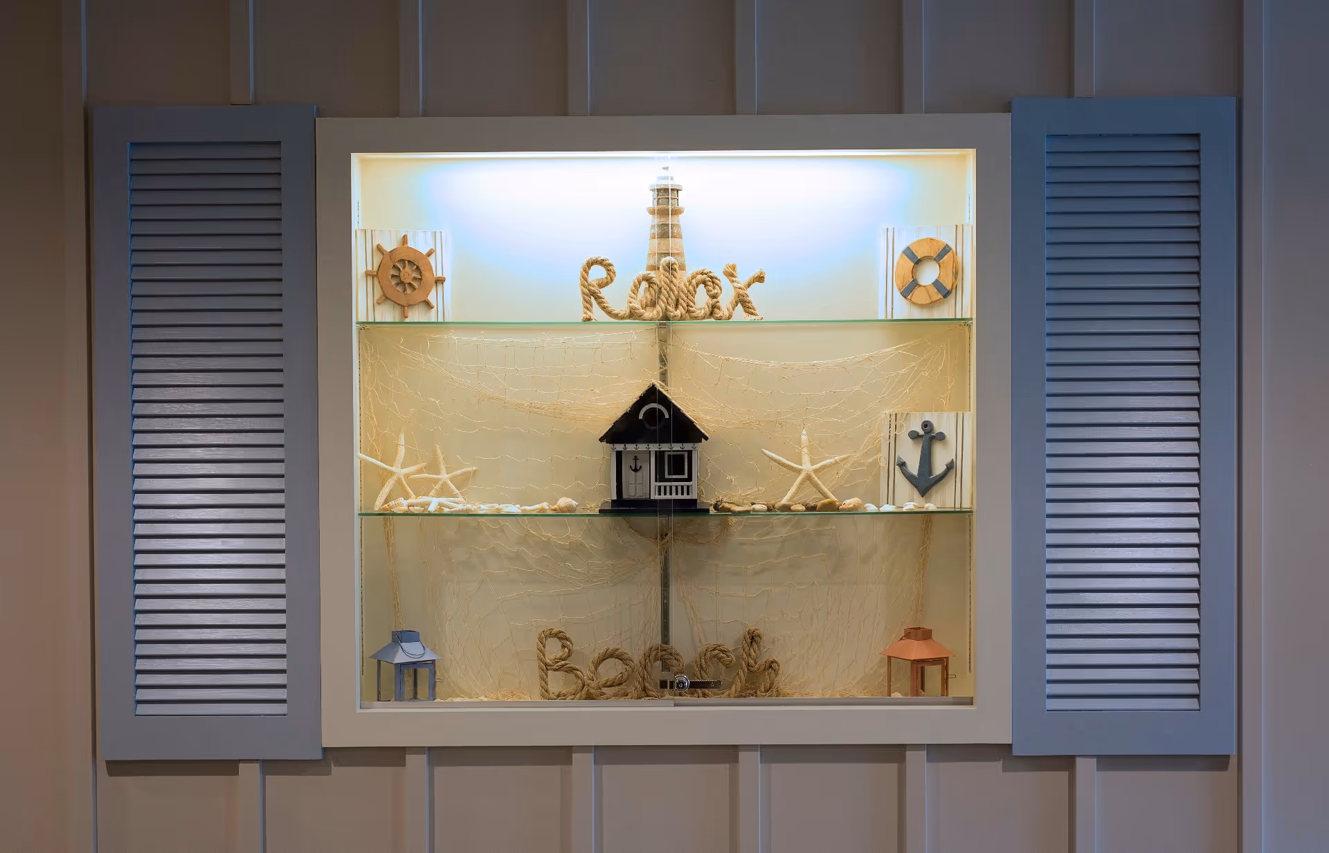 Wall niche with glass shelves displaying nautical-themed decorations including a lighthouse, starfish, an anchor, and a rope 'Relax' sign.