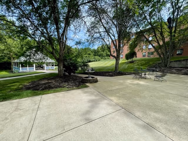 Outdoor courtyard with a gazebo, small fountain, patio seating, trees, and a brick building in the background.