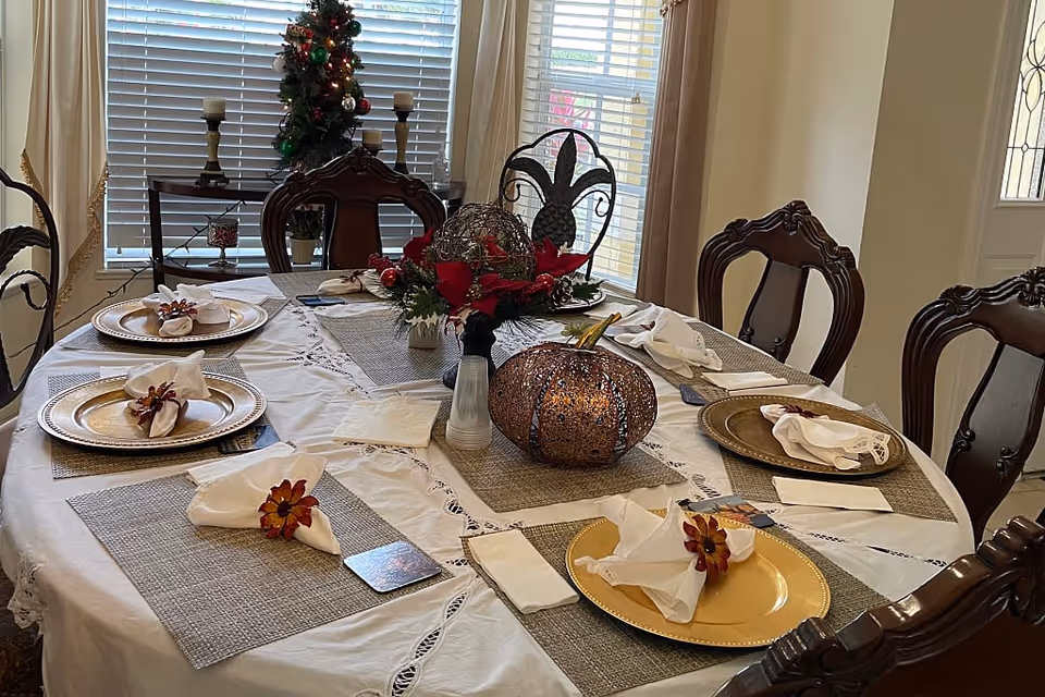 A dining table set with gold chargers, folded napkins, and a decorative centerpiece including a pumpkin and flowers in a dining room.