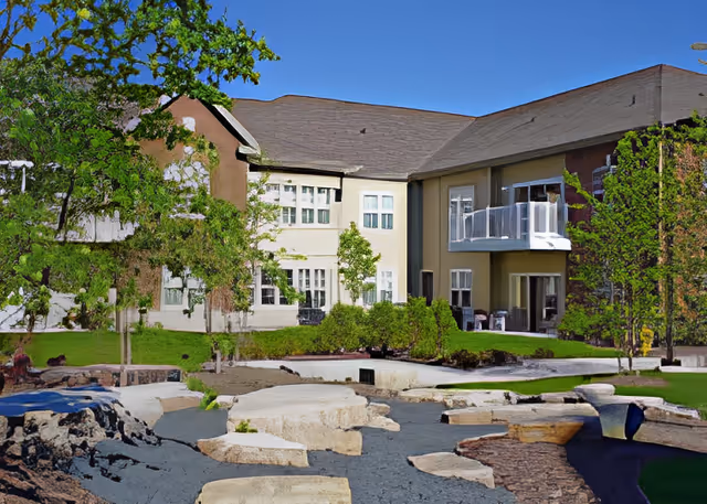 Exterior view of the Covenant Living of the Great Lakes building with landscaped courtyard, stone pathways, trees, and balconies.