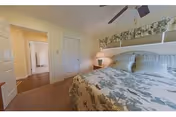 Bedroom with a floral-covered bed, nightstand and lamp, ceiling fan, and a hallway leading to other rooms.