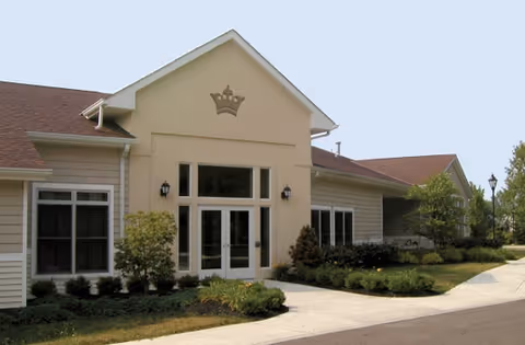 Front entrance of a single-story facility with double glass doors, landscaping, and a crown emblem above the doorway.