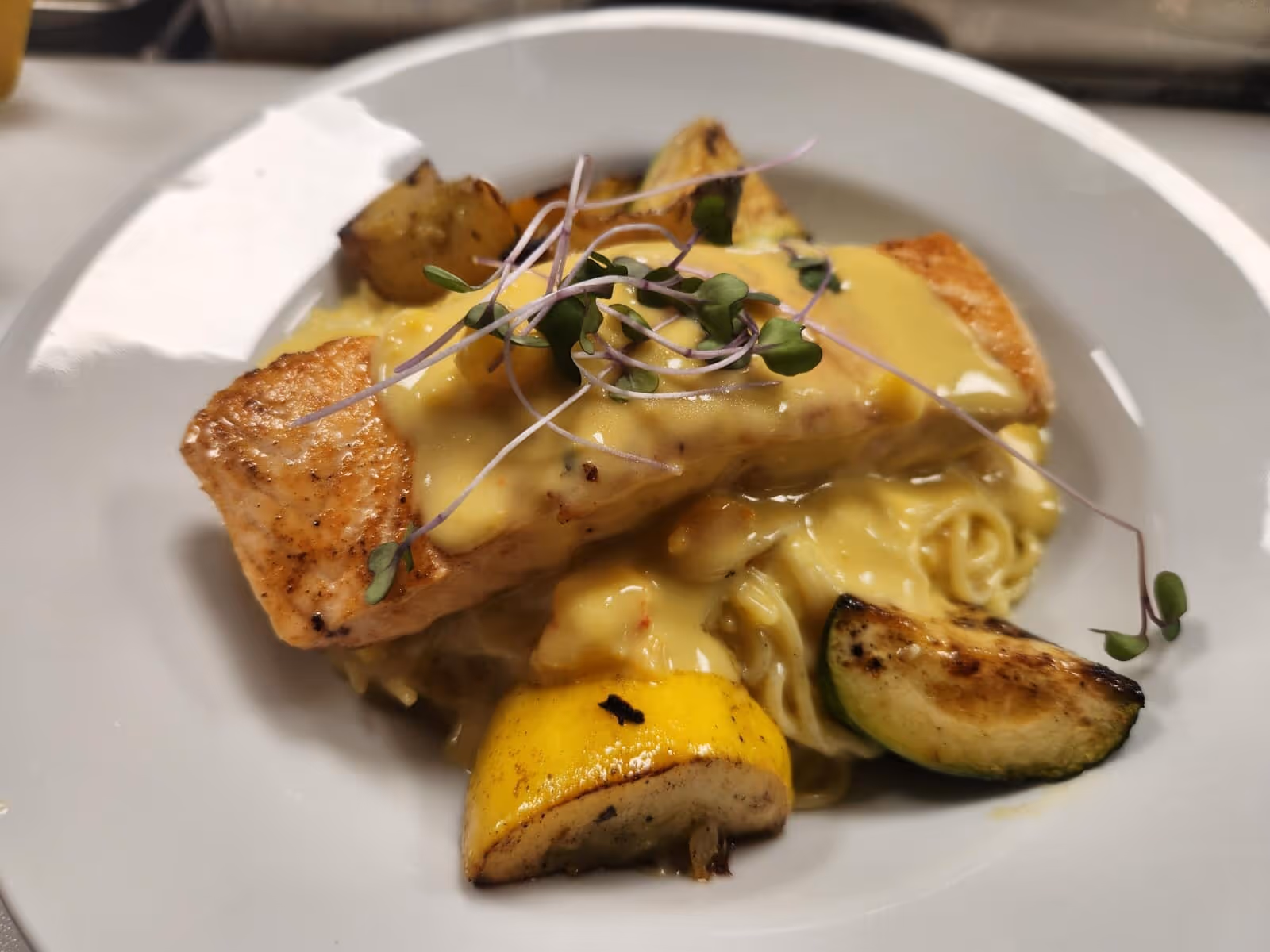 A plated dish featuring salmon with a creamy sauce, served with vegetables and pasta.