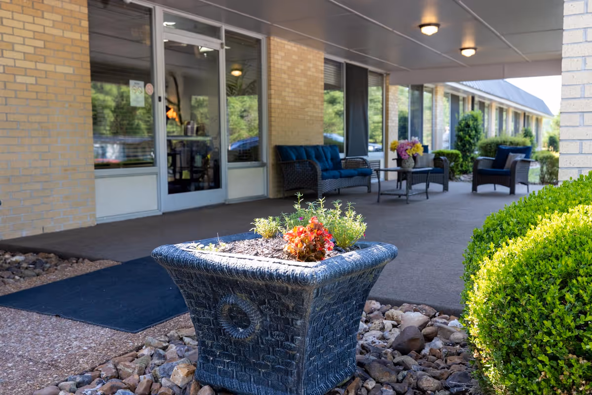 Covered entrance patio with a decorative planter in the foreground and cushioned outdoor seating by glass doors.
