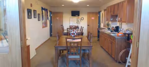 Interior dining room in a senior living facility with a central wooden table and chairs.