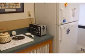 A small kitchenette with a two-burner electric cooktop, toaster oven, kettle on the counter and a white refrigerator.