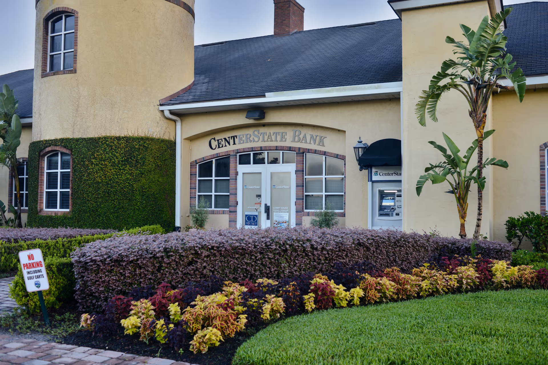 Front exterior of a yellow stucco building with a CenterState Bank entrance, ATM, and landscaped shrubs.