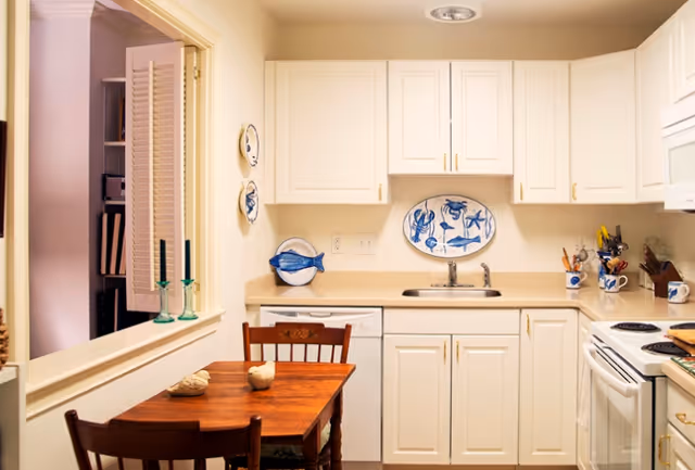 Small kitchen with white cabinets, a sink and stove, and a wooden dining table with chairs.