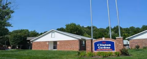 A brick senior living facility exterior with a Clinton Gardens sign in front.