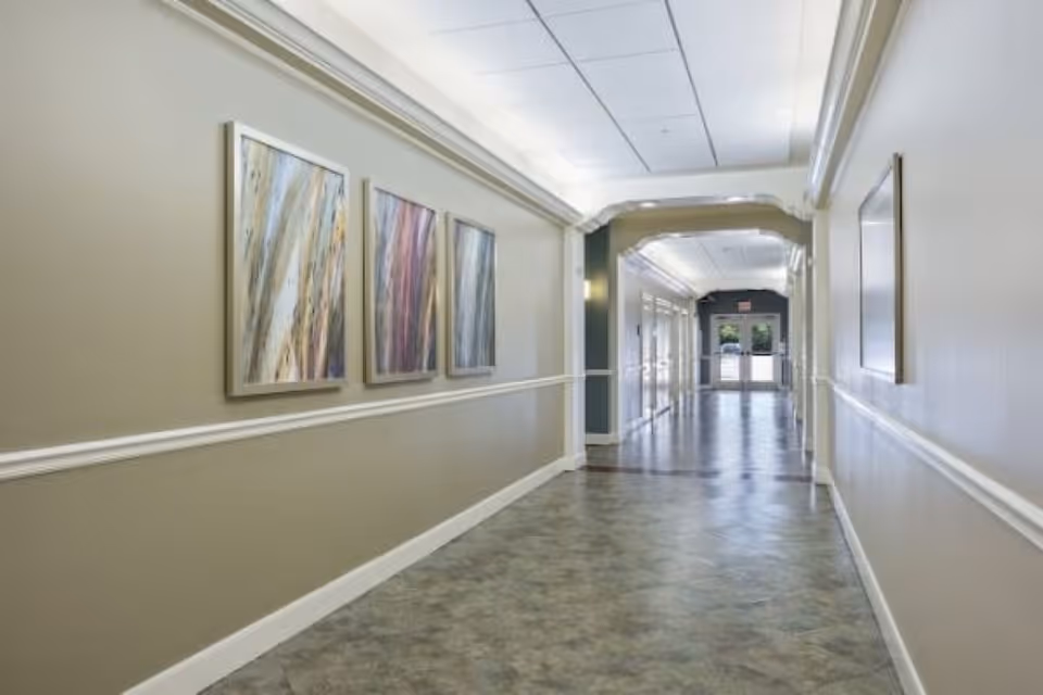 Long, well-lit interior hallway with framed artwork along the left wall and a doorway at the far end.