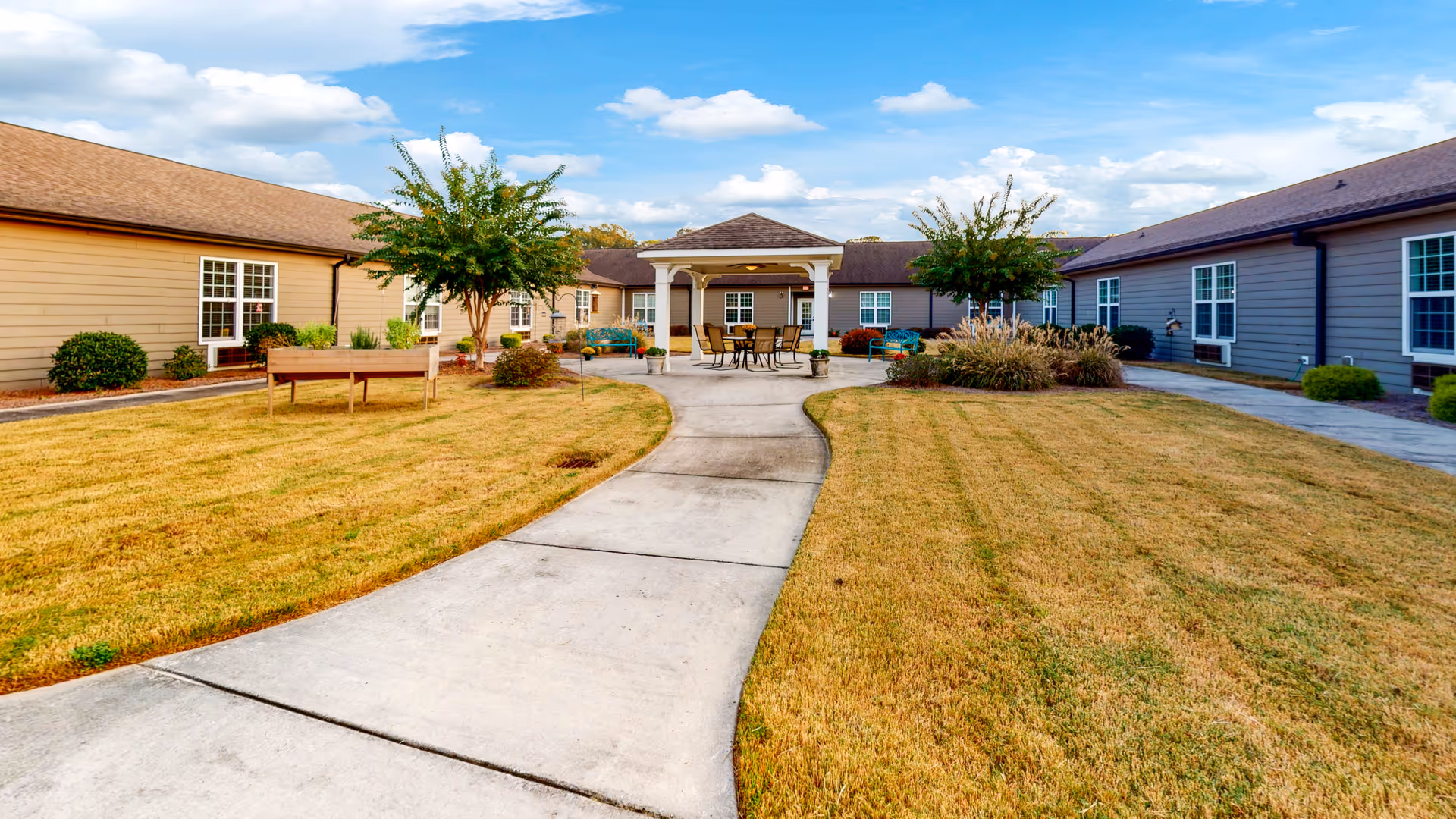 Central paved walkway leading to a covered patio in a landscaped courtyard flanked by single-story residence buildings.