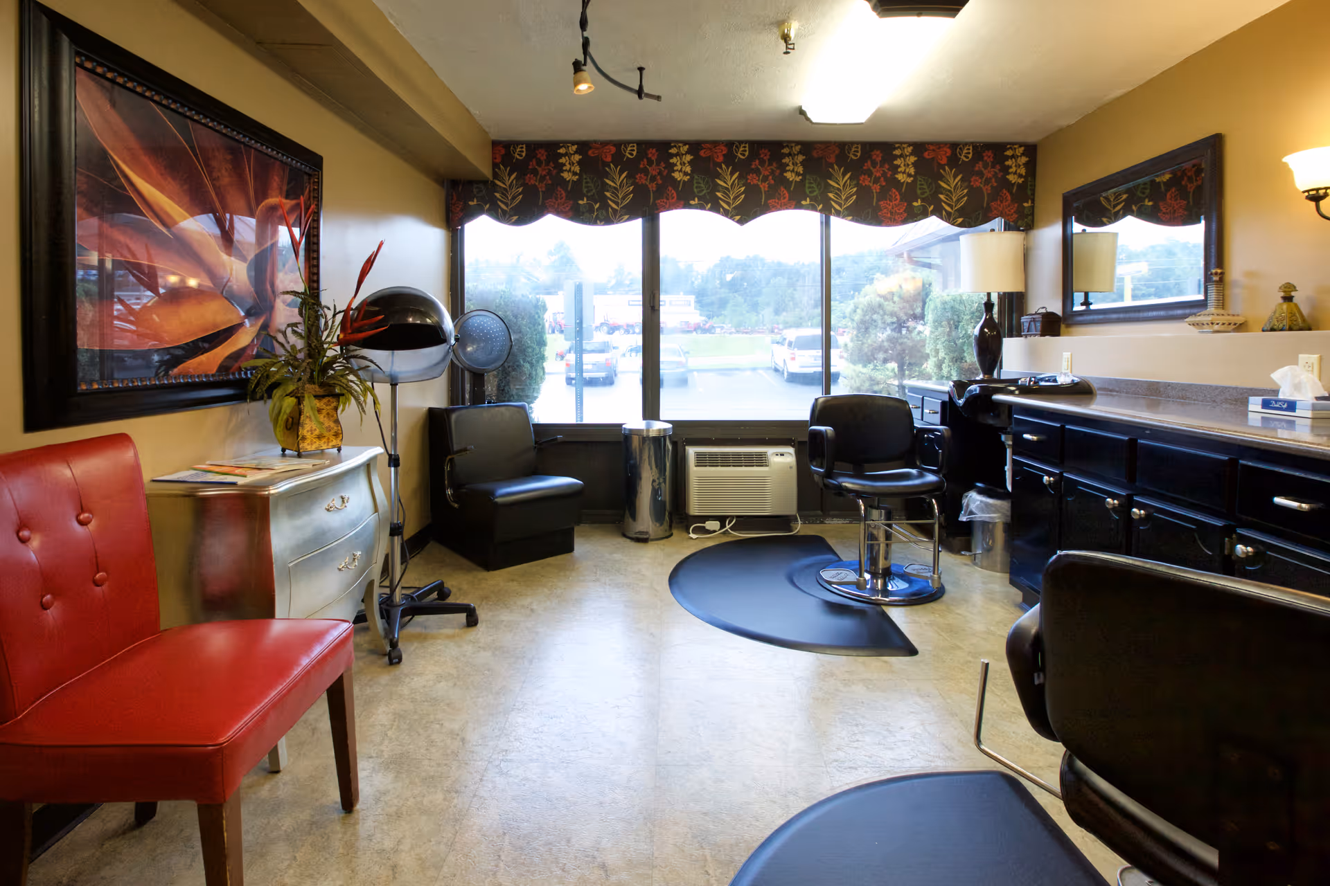 Small salon room with styling chairs, a hooded hair dryer, mirrors, and large front windows.