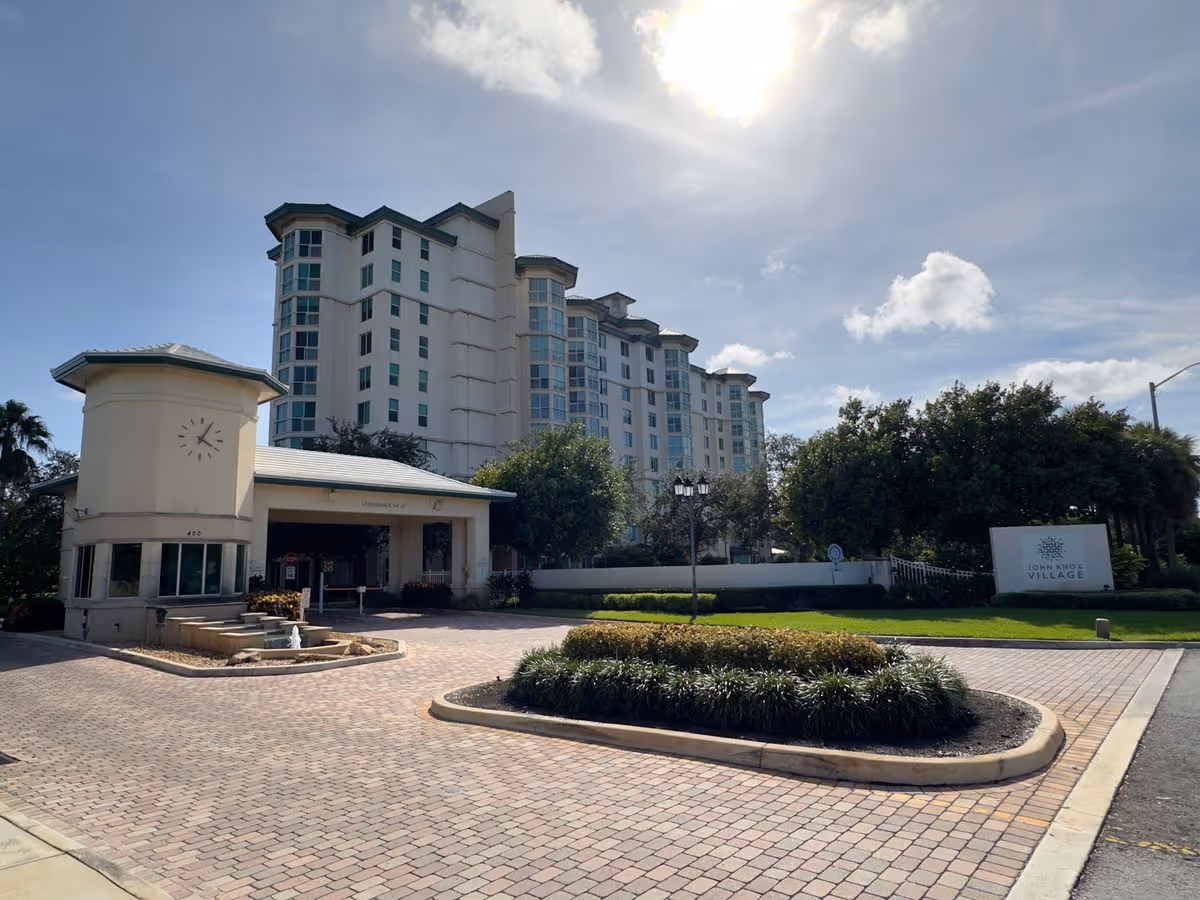 Front entrance and multi-story residential building of John Knox Village with a circular driveway, fountain, and landscaping.