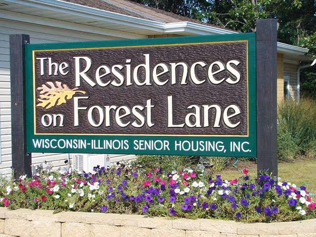 Front exterior sign for The Residences on Forest Lane with colorful flowers.