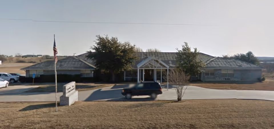 One-story brick building with a covered entrance, flagpole and front sign on a grassy lawn with a vehicle in the driveway.