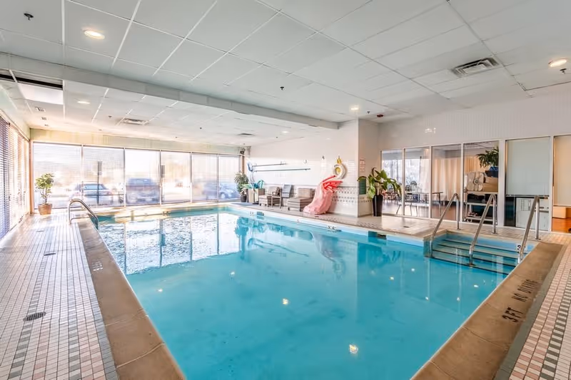 Indoor swimming pool with seating area, plants, large windows, and pool steps.