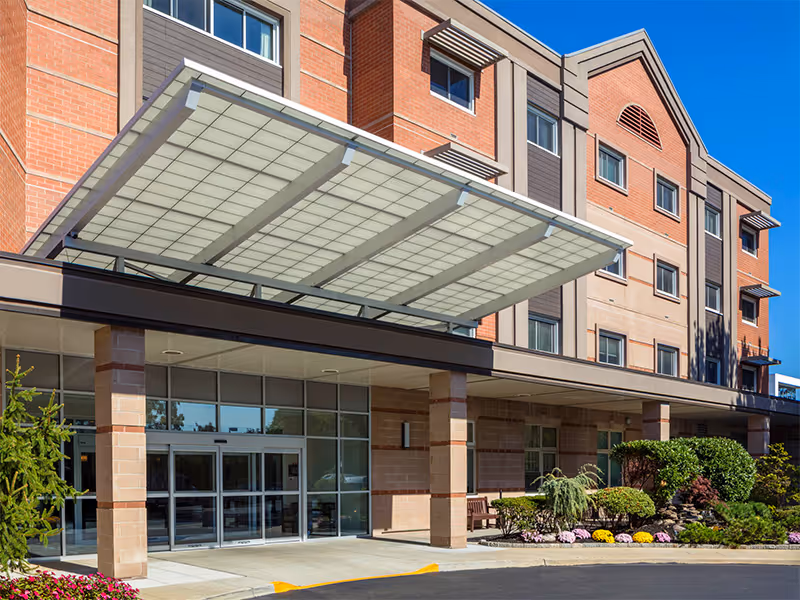 Exterior view of Atria Park of Lynbrook entrance with glass doors and a covered canopy.