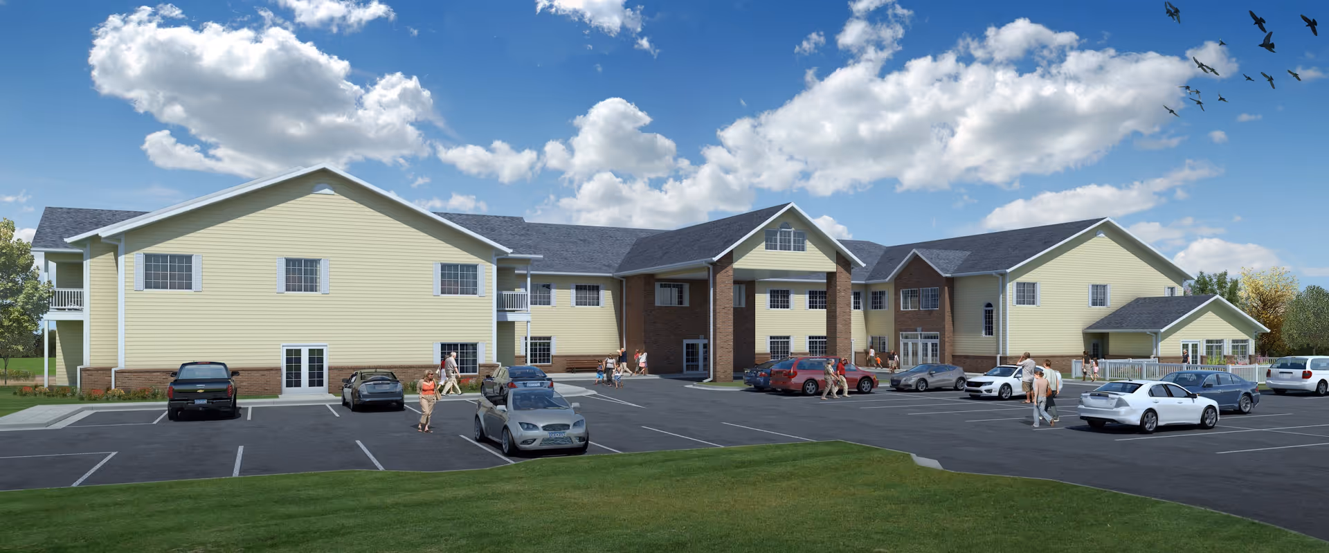 Exterior view of a large two-story senior living facility building with yellow siding and brick accents. Several cars are parked in the parking lot in front of the building, and a few people are walking near the entrance. The sky is blue with scattered clouds and birds flying overhead.