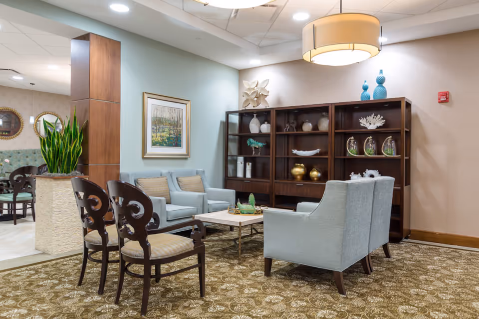 A furnished communal lounge with armchairs, decorative shelving, and a coffee table.