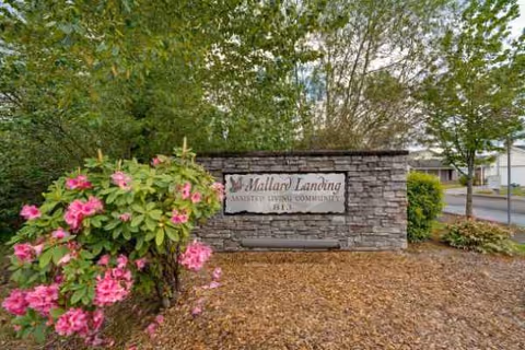 Stone entrance sign for Mallard Landing Assisted Living Community flanked by flowering shrubs outdoors.